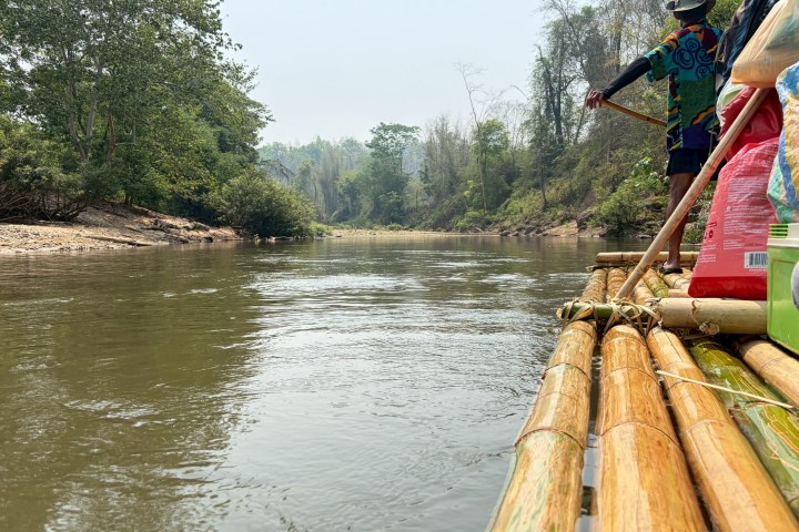 Person navigating bamboo raft down a calm river surrounded by lush greenery.