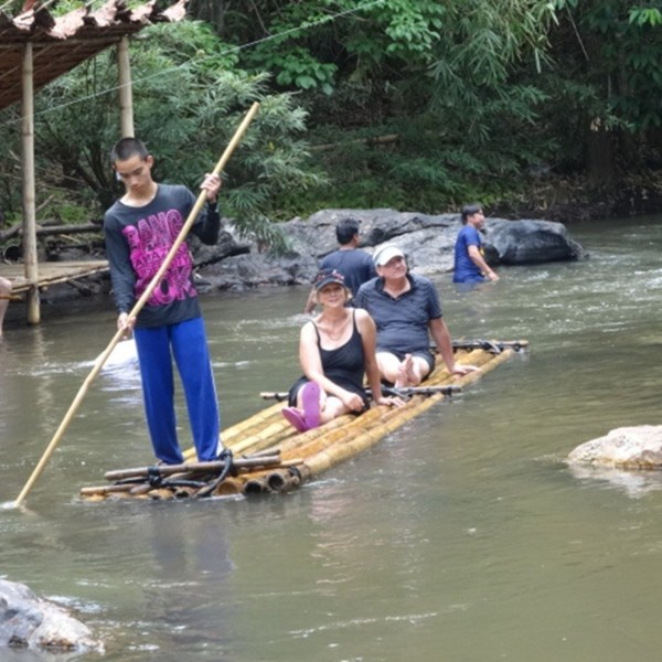People riding a bamboo raft on a small river with lush greenery.