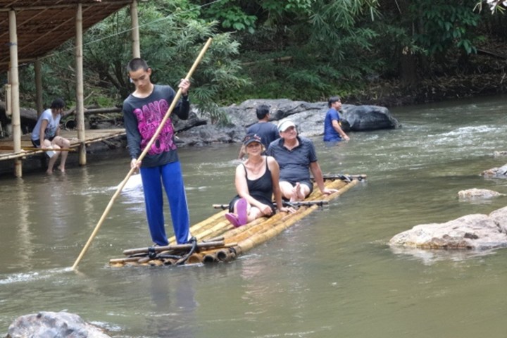 People riding a bamboo raft on a small river with lush greenery.