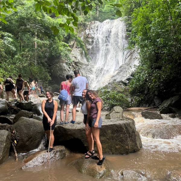 People standing on rocks near a waterfall in a forested area.