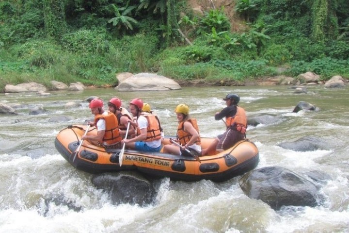 Group rafting in an orange inflatable boat on a rocky river.