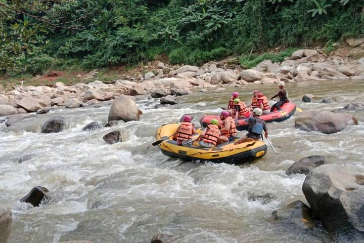 Group rafting on a rocky river amidst lush greenery.